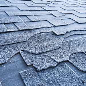 Close up view on Asphalt Roofing Shingles roof damage covered with frost.